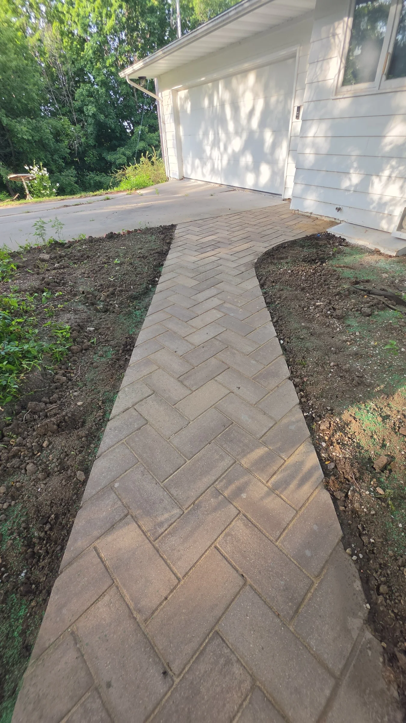 Completed interlocking-paver walkway leading through planting beds to a residential garage entrance