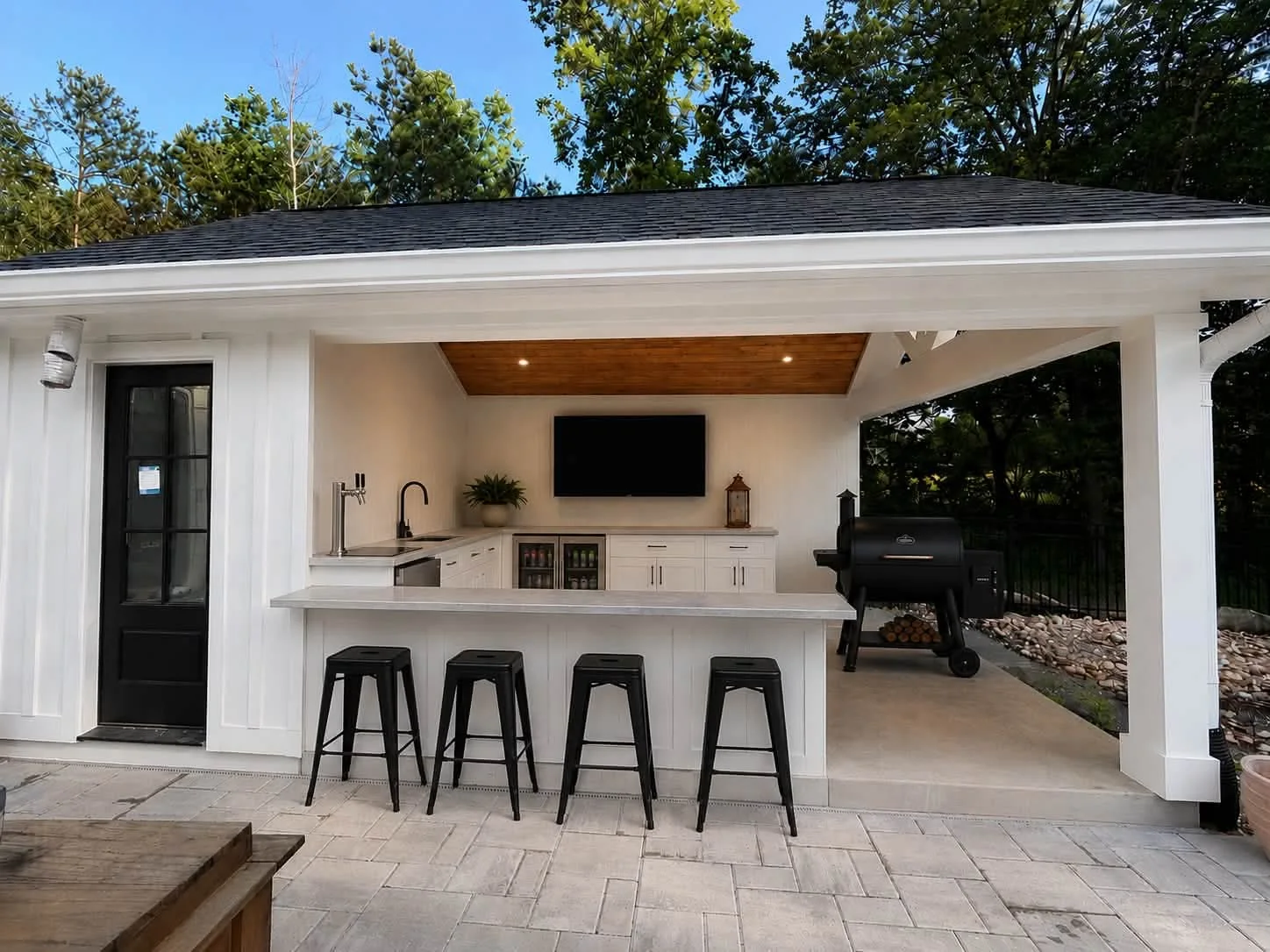 Finished covered patio with an outdoor kitchen, built-in bar, stools, sink, grill, cabinetry, and television