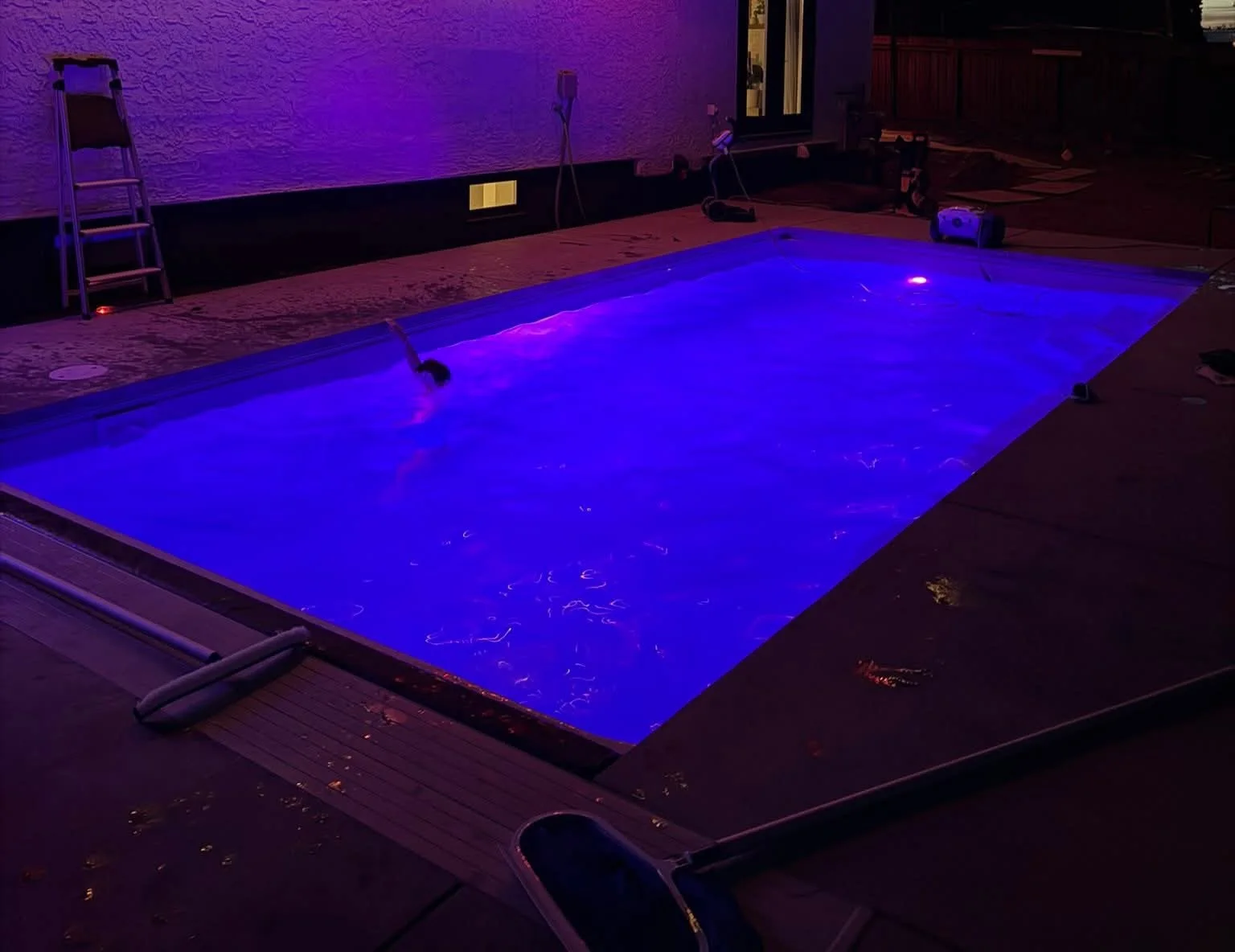 In-ground pool illuminated blue at night with a surrounding deck