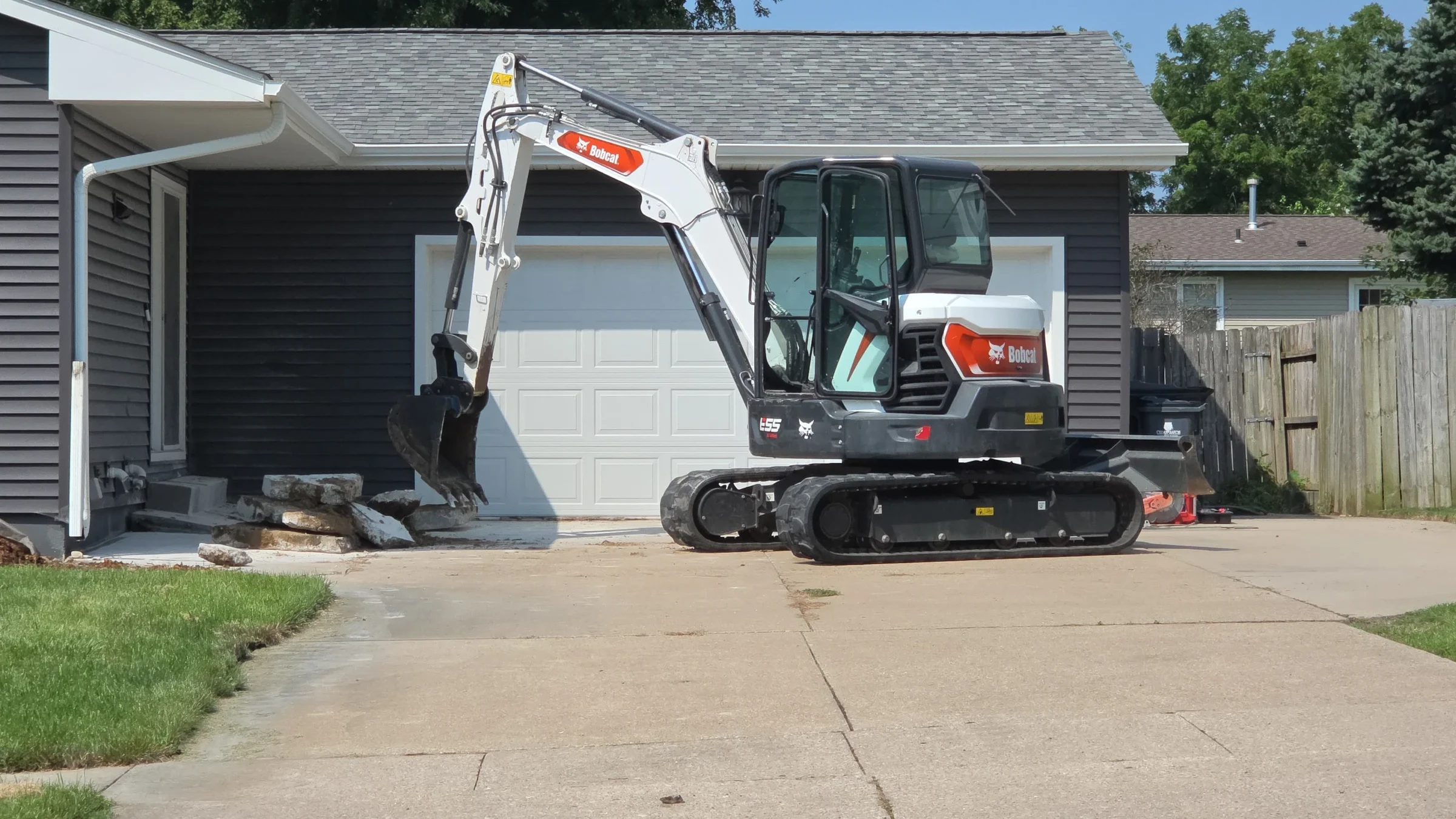 Tracked compact excavator parked on a residential driveway beside a garage