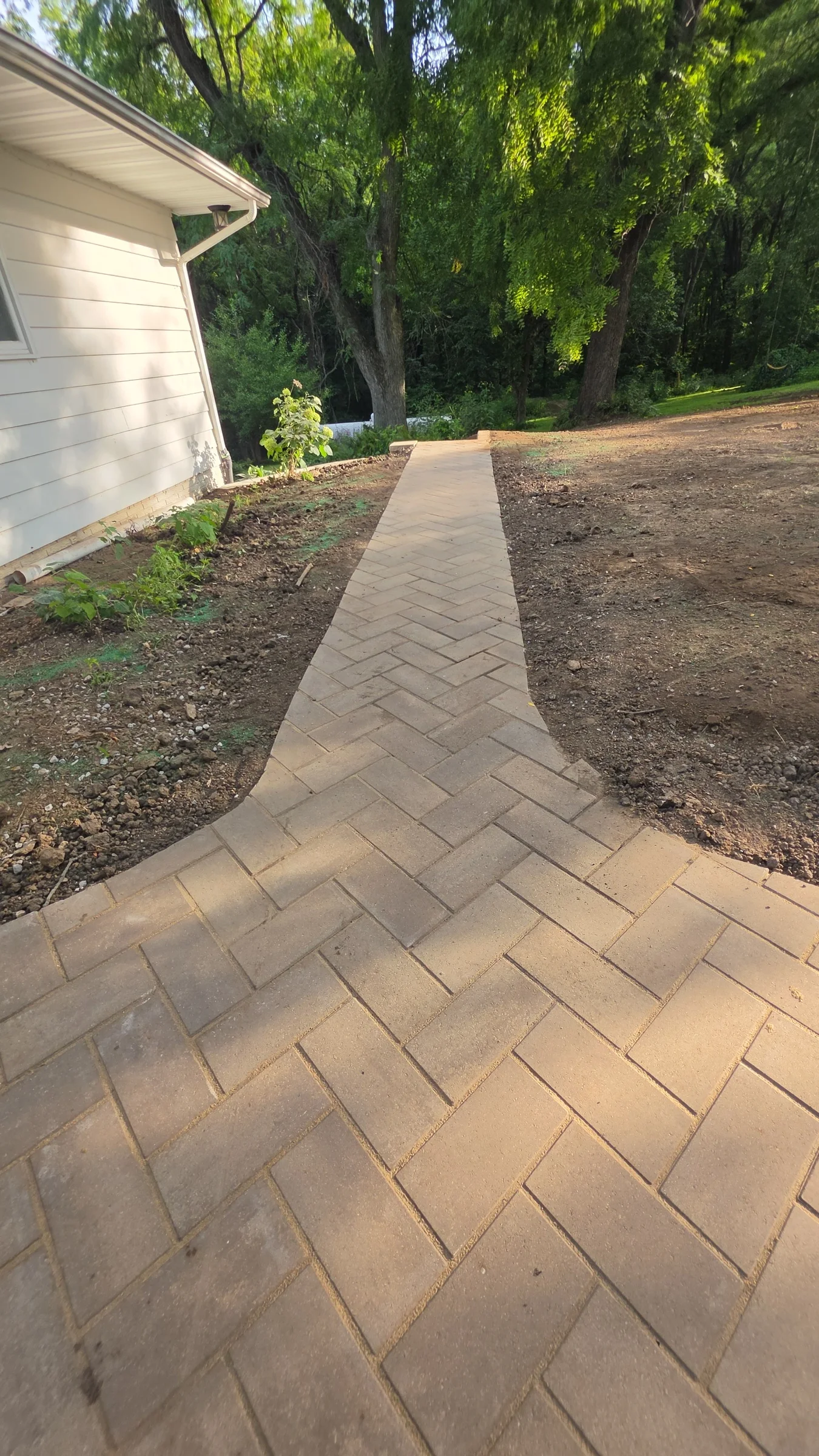 Completed interlocking-paver walkway and adjoining hardscape surface beside a residential home