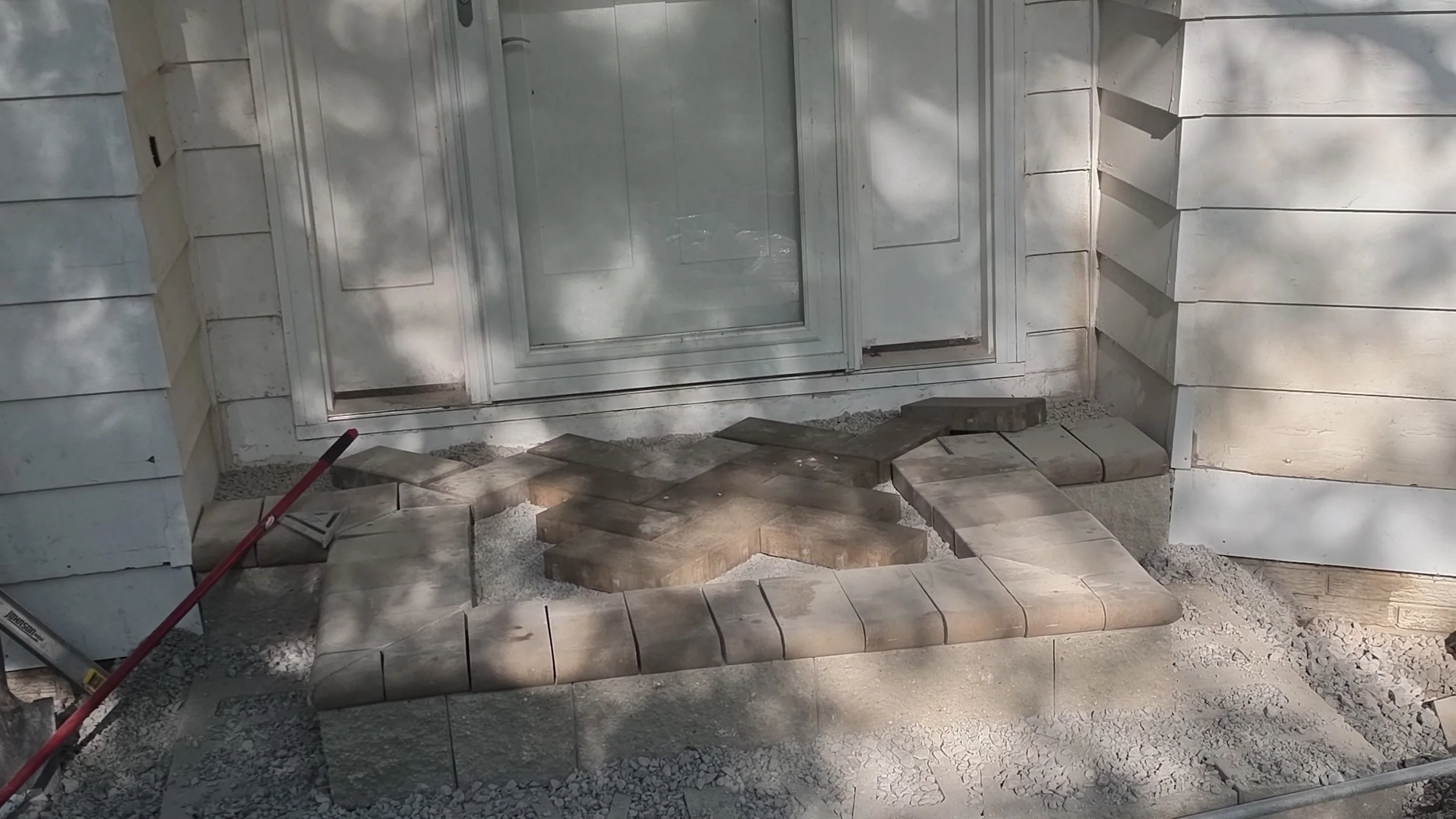 Paver walkway and edging layout on a prepared stone base beside a residential garage entrance
