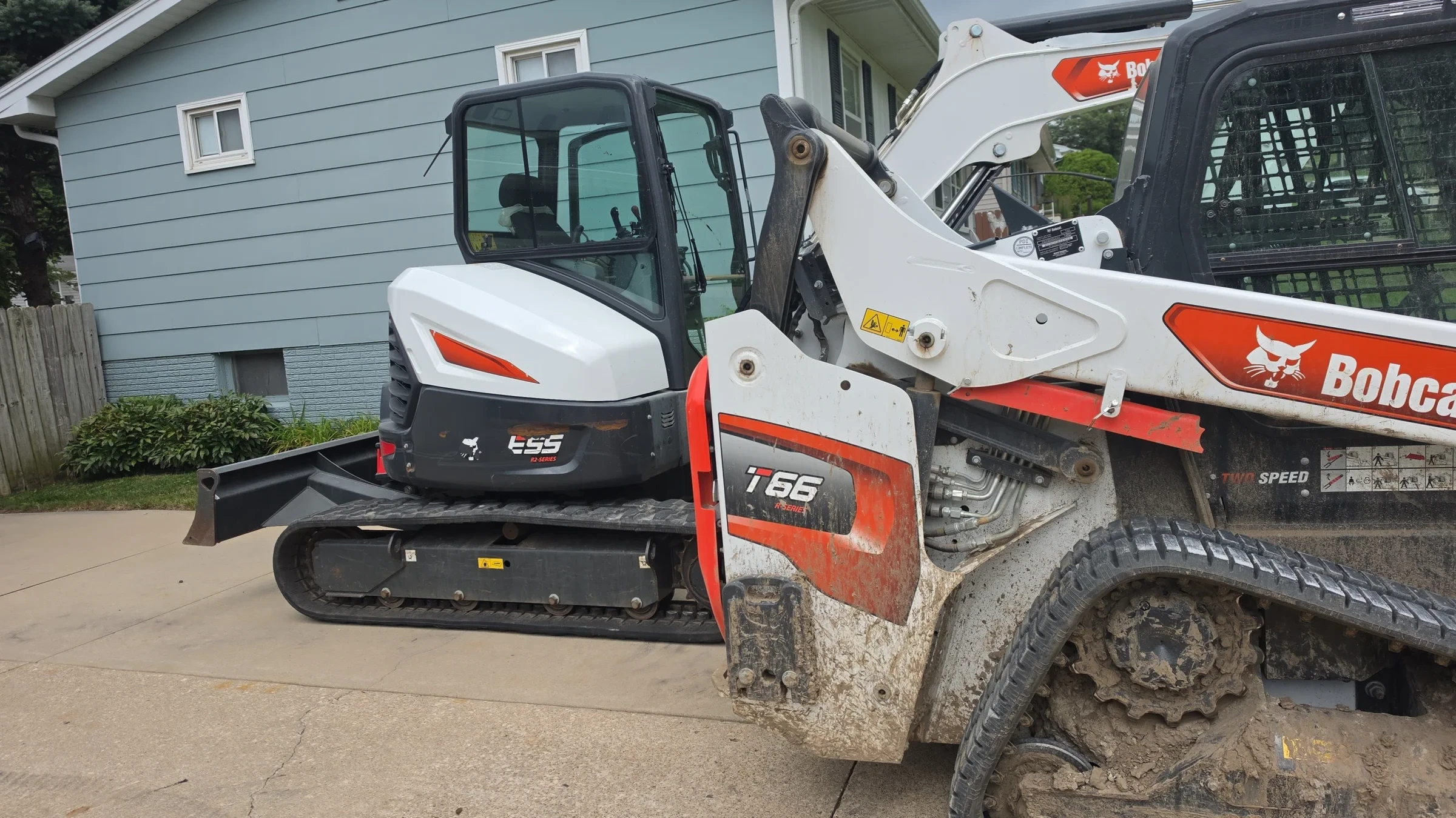 Compact excavator and track loader parked beside a residential building